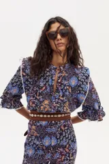 Camisa estampada con flores y motivos geométricos en tonos azules, marrones y naranjas. Tiene cuello mao, mangas 3/4 con volados y detalles de encaje en los hombros y mangas.