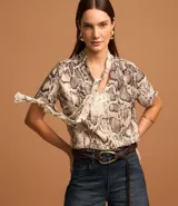 Blusa de chiffon con estampado de serpiente en tonos beige y marrón. Tiene cuello alto con lazo y mangas cortas.