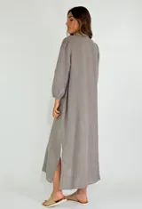 Vestido largo color beige de lino, con cuello mao, mangas 3/4 abullonadas y cierre frontal con botones. Presenta volantes verticales en el frente.