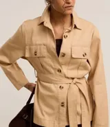 Campera trench coat color beige, con cuello inglés, manga larga, abotonado delantero, bolsillos con solapa y lazo en la cintura.