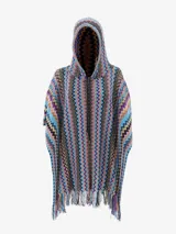 Poncho de tejido de punto con capucha y cierre frontal parcial. Presenta un patrón de zigzag multicolor vibrante con predominancia de tonos azules, morados, naranjas y negros. El borde inferior tiene flecos largos.