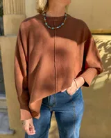 Sweater de punto color terracota, con diseño holgado, cuello redondo y aberturas laterales en el ruedo. Presenta puños acanalados y una etiqueta decorativa en la parte inferior.