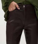 Pantalón flare de poliuretano con diseño de cinco bolsillos, trabillas para cinturón, cierre frontal y recortes horizontales en las rodillas. Presenta un corte ajustado en la parte superior con piernas levemente acampanadas hacia el ruedo.