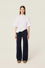 Jean de corte recto y tiro medio, confeccionado en tejido vaquero de color azul marino oscuro con un sutil patrón de rayas verticales. Presenta costuras en contraste, cierre de botón metálico y detalle de insignia de cuero en la parte posterior.