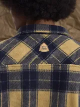 Sobrecamisa de tejido polar con estampado abstracto en tonos rojizos y azul marino. Presenta cuello clásico, cierre frontal con botones a presión, dos bolsillos frontales con solapa en el pecho y un parche decorativo.