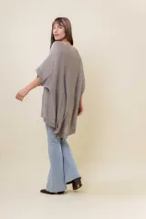 Maxi sweater tejido color beige con efecto metalizado sutil, silueta amplia, mangas tipo murciélago y largo asimétrico (más corto adelante y más largo atrás).