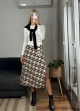 Pollera midi de corte recto con tajo lateral, confeccionada en tela con estampado escocés en tonos marrones, blancos y negros.