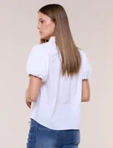 Camisa blanca de calce recto confeccionada en algodón elástico, con cuello mao, abertura frontal en V y cartera con botones ocultos. Presenta mangas cortas abullonadas con puños elastizados y ruedo redondeado.