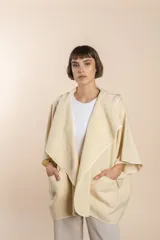 Ruana color crudo de lana fina sin teñir, con capucha, bolsillos y terminaciones envivadas. Tiene un broche para usar cerrada. Es una prenda oversize sin forro, cómoda, versátil y fácil de combinar.
