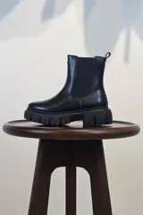 Bota tipo Chelsea de caña corta en color beige, confeccionada en material sintético con acabado liso. Presenta paneles elásticos laterales a tono y una suela track robusta y dentada que aporta altura y estilo moderno.