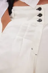 Pantalón de jean con diseño de tiro medio-bajo y piernas anchas. Presenta una pretina ancha con cierre de tres botones metálicos frontales, pinzas decorativas en la cintura y bolsillos delanteros funcionales.