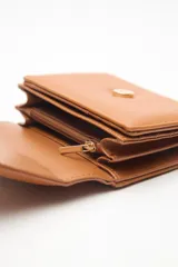 Billetera compacta de cuero sintético negro, con solapa que combina texturas lisas y efecto reptil. Incluye un aplique metálico circular con logo grabado en el frente y cierre con broche.