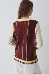 Remera tejida de punto estilo polo con mangas largas en color crema y cuerpo en color bordó con rayas verticales amarillas. Presenta cuello tipo polo, aberturas laterales y un pequeño parche circular con diseño de sol en el pecho.