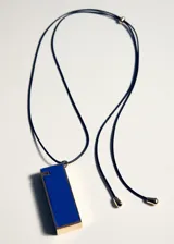 Collar largo con cordón negro ajustable y un dije colgante rectangular con detalles metálicos dorados y resina en tono azul.