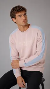 Buzo de cuello redondo en color rosado con franjas laterales en color celeste. Presenta el logo de la marca bordado en el pecho y puños elásticos.