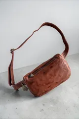 Riñonera de cuero terracota con diseño pintado a mano en tonos turquesa y dorado, con cierre superior y correa ajustable con herrajes metálicos.
