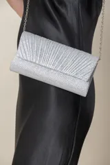Cartera tipo sobre de fiesta en color plateado, confeccionada en material con acabado de lúrex brillante. Presenta un diseño frontal plisado y cuenta con una cadena metálica fina para colgar al hombro.