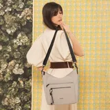 Cartera bandolera gris de formato amplio, con correa larga regulable y desmontable con inscripciones. Cuenta con cierre superior, bolsillo frontal con cierre y detalle colgante de cordones, y un bolsillo trasero con cierre.