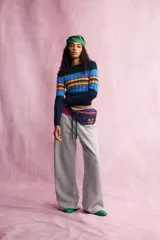 Riñonera violeta con detalles en naranja, perteneciente a la colección especial Fruit of the Loom x Zara. Cuenta con un compartimento principal y un bolsillo frontal con cierre de cremallera metálica, además de un bordado distintivo en la parte inferior. Incorpora un cinturón ajustable con cierre de clip de plástico negro.