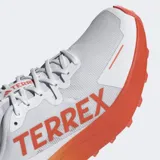 Championes de trail running Adidas Terrex Agravic 3 en color blanco con detalles en naranja. Presentan una mediasuela Lightstrike para amortiguación dinámica, suela de caucho Continental™ con perfil dentado para tracción en senderos y exterior textil transpirable con refuerzos sintéticos resistentes a la abrasión.