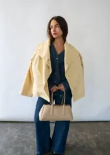 Campera de algodón color amarillo manteca, con cuello alto, cierre frontal con botones metálicos y cinturón ajustable en la cintura. Presenta un diseño versátil que permite llevarla entallada o con silueta holgada.