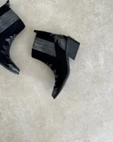 Botín de cuero vacuno negro, con caña corta, taco cuadrado y detalles de apliques metálicos. Diseño de estilo western con puntera fina y apliques en forma de llamas. Horma chica.