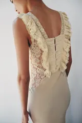 Vestido largo color beige de viscosa, con escote cuadrado, tirantes anchos, detalles drapeados, volantes y aplicaciones de encaje a contraste en el pecho. Cuenta con cierre trasero de botones.