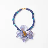 Collar de cuentas de resina en tonos azul y turquesa, con un dije central grande en forma de flor de pétalos jaspeados en tonos violeta y azul con centro amarillo.