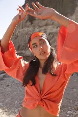 Blusa color naranja con escote en V, mangas largas acampanadas y nudo en la parte delantera.