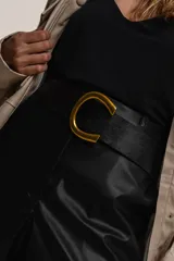 Cinto negro de cuero sintético con hebilla dorada en forma de letra C.