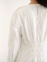 Vestido largo blanco de manga larga, cuello redondo y corte recto, con detalle de textura vertical y aberturas laterales en el bajo.