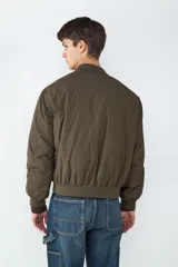 Campera tipo bomber acolchada en color verde militar, con cuello redondo, cierre frontal de cremallera metálica y bolsillos laterales con cierre. Presenta puños y bajo elásticos para un ajuste cómodo.