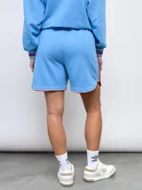 Short de felpa celeste, de corte deportivo, con detalles de pipings tricolor en los bordes y escudo del Club Nacional de Football aplicado en la pierna.