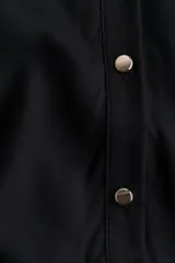 Vestido midi negro con cuello camisero, botonadura frontal de botones dorados, mangas cortas y cinturón ajustable para atar en la cintura.