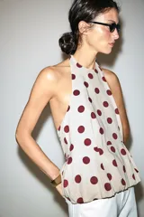 Top beige con estampado de lunares bordó, cuello halter, diseño sin mangas y bajo con volantes. Cuenta con cierre de lazada en la espalda.