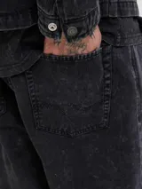 Pantalón de corte baggy y tiro alto, confeccionado en denim con efecto lavado ácido en color negro. Presenta una silueta amplia y relajada, con bolsillos funcionales y cierre frontal.