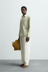 Camisa de hombre de corte relajado (relaxed fit) en color verde menta pálido, confeccionada en tejido con textura irregular acanalada. Presenta cuello solapa, manga larga con puño abotonado, bolsillo plastrón en el pecho y bajo asimétrico con aberturas laterales.