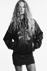Chaqueta bomber de efecto piel en color marrón oscuro, con cuello solapa, cierre frontal de cremallera metálica, bolsillos laterales de vivo y mangas largas con puños elásticos. El bajo cuenta con ajuste elástico.
