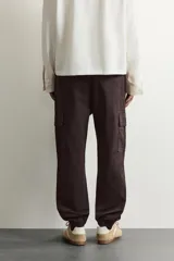 Pantalón cargo de corte ajustado en color negro, confeccionado en tejido de algodón con elasticidad. Presenta cintura elástica con cordón ajustable, bolsillos laterales tipo cargo con solapa y bajo con puños elásticos.