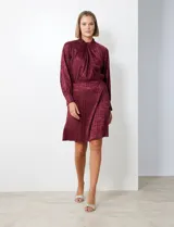 Vestido corto color borgoña con estampado geométrico, de gasa laminada con cuello alto entrelazado, manga larga raglán, cintura elastizada y espalda con abertura ojal y botones.