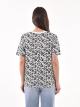 Remera de manga corta color beige con estampado de bananas en tonos amarillo, naranja y rosado.