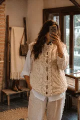 Chaleco de lana natural tejido a mano, con diseño de trenza central artesanal y aberturas verticales. Presenta una silueta relajada y cuello redondo.