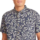 Camisa de manga corta con estampado de flores abstractas en tonos beige sobre fondo azul. Tiene cuello clásico, cierre frontal con botones y bolsillo en el pecho.
