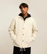 Campera color crema de poliéster con cuello inglés, abotonadura delantera con botón a presión, mangas largas con puño elástico, bajo elástico y cordón para ajustar.