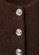 Chaqueta entallada de tejido bouclé color marrón, con cuello redondo, manga larga y cierre frontal de botones con efecto joya. Incluye forro interior.