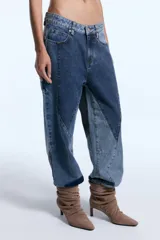 Pantalón de jean con diseño de patchwork que combina diferentes tonos de denim en paneles geométricos. Presenta un corte relajado, tiro medio y cierre frontal con botón metálico.