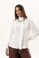 Camisa blanca de cuello alto con volados frontales a lo largo de la botonadura, manga larga con puños con volados y cierre frontal con botones.