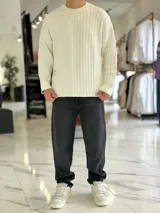 Sweater de punto oversize color marrón, con cuello redondo y diseño combinado: la mitad derecha cuenta con tejido de ochos y la izquierda es lisa. Incluye una etiqueta decorativa blanca en el frente inferior derecho.