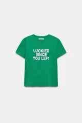 Camiseta verde de corte regular fit, con cuello redondo, manga corta y efecto lavado. Cuenta con un estampado de texto en color blanco en el centro del pecho que dice "LUCKIER SINCE YOU LEFT".