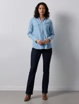 Camisa de manga larga en tela denim de color azul medio, con cuello clásico, botones frontales y dos bolsillos de parche con solapa en el pecho.